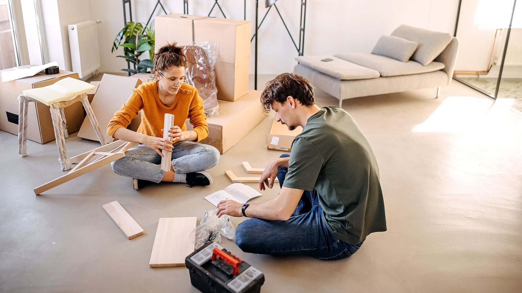 A woman and a man sit on the floor and assemble a chair together.