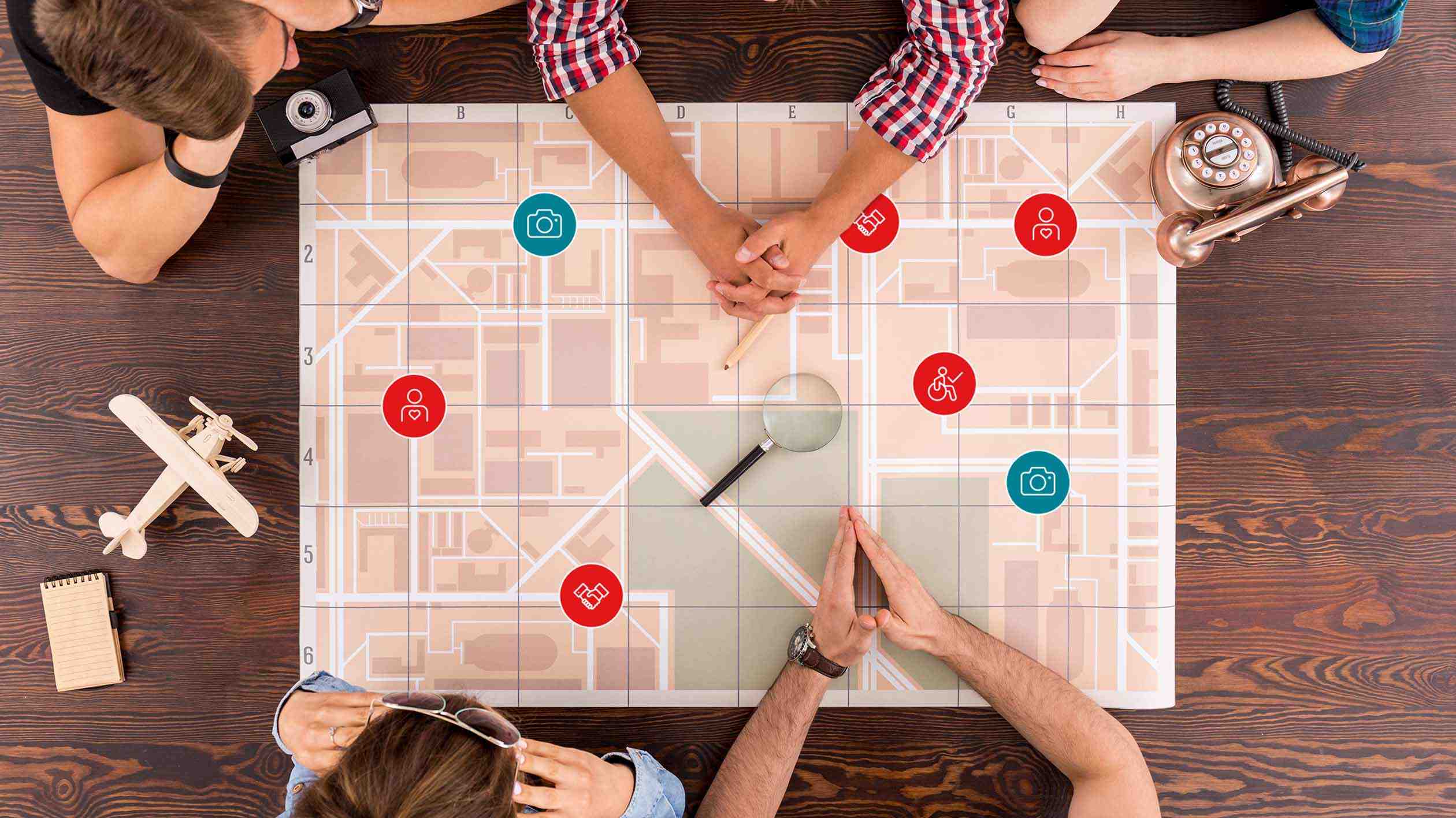 View from above of a table at which several people are sitting: On the table is a large, abstract road map