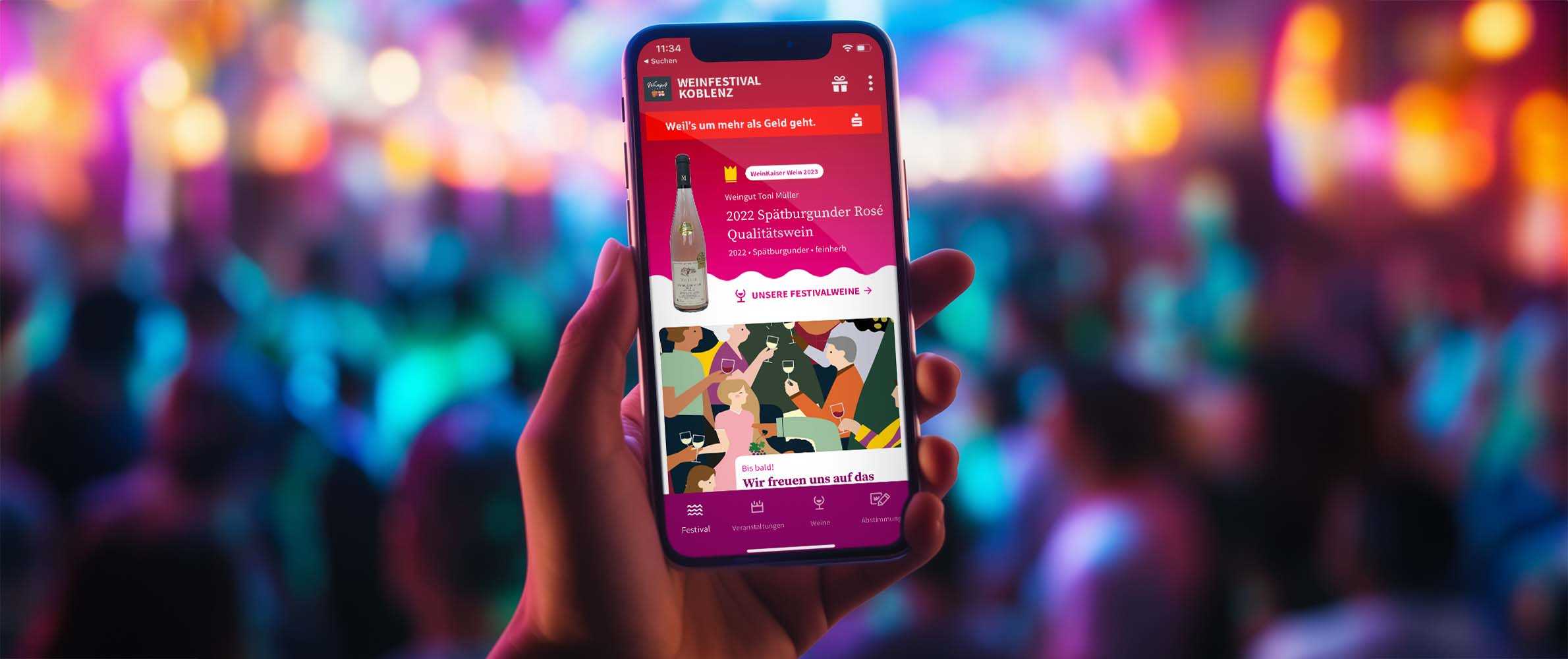 Eine Hand hält ein Smartphone, das die Wein App zeigt. Im Hintergrund sind verschwommene bunte Lichter bei Nacht zu sehen.