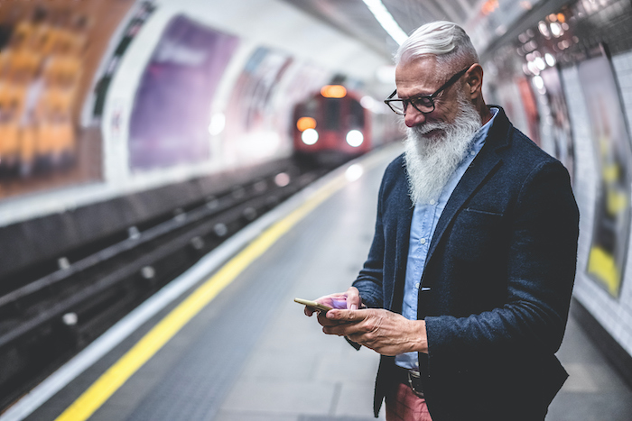 A man in a subway station holding a smartphone while a train is entering the station