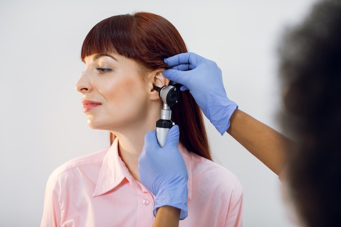 Eine Frau, deren Ohr beim Arzt mit einem Gerät untersucht wird