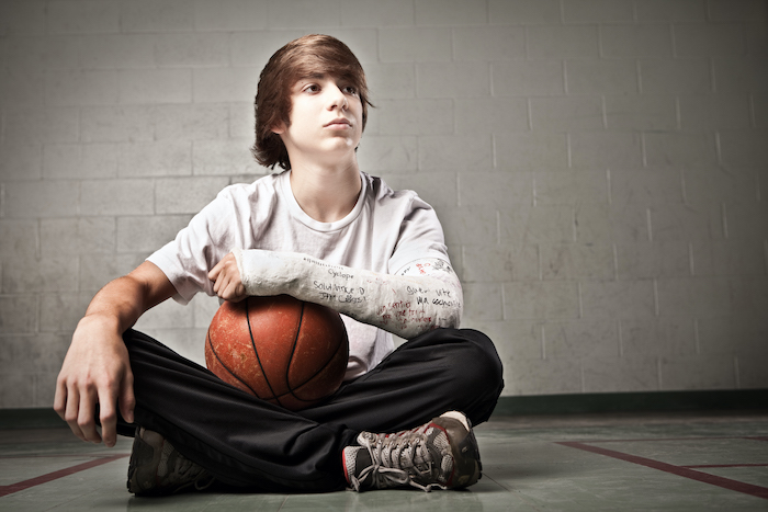 A young person sitting cross-legged on the floor with a broken arm and a basketball